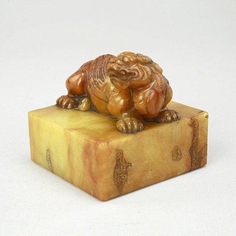 CHINESE CARVED SOAPSTONE STAMP: With an intricately carved recumbent foo dog atop a square block, with the head turned to its side and mouth slightly opened, with a fine detail of the mane running from the head to the back of the bo