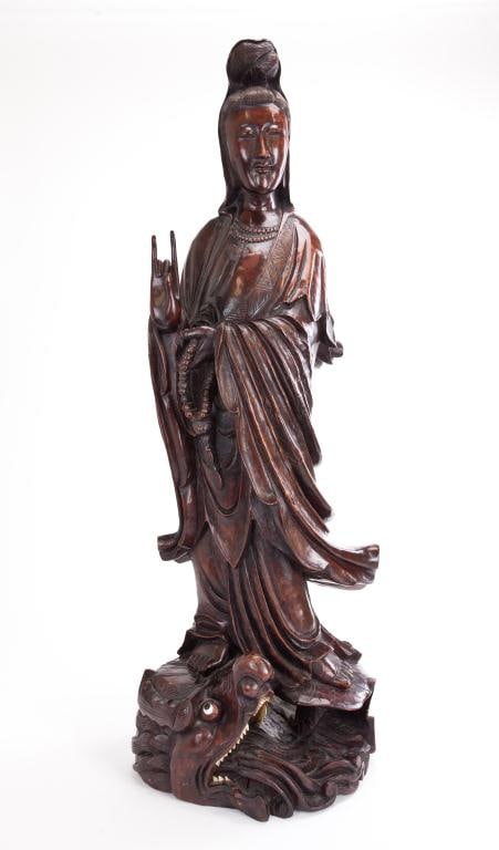 ANTIQUE CHINESE CARVED WOOD GUANYIN: Carved of a slender form, she wears a flowing robe and has her right hand in Karana mudra. She holds prayer beads in her left hand and stands atop a lily pad base on a dragon's head. H: 36 in.