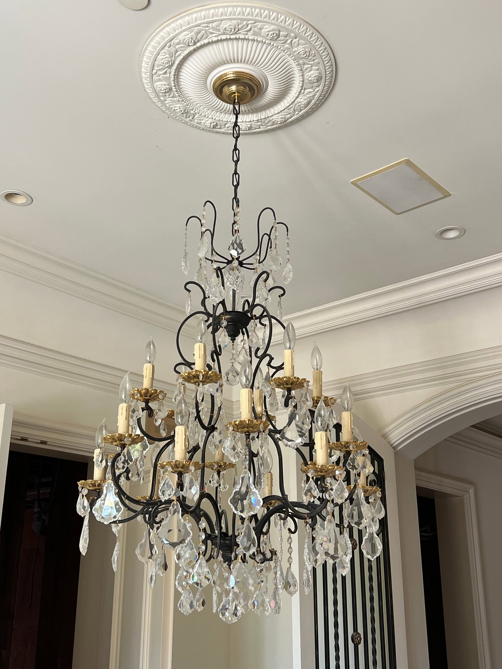 18-LIGHT WROUGHT IRON AND CUT CRYSTAL CHANDELIER: Dimensions: H: 14in. x W: 32in.A large eighteen-light wrought iron chandelier executed in a Baroque or Rococo Revival style, featuring scrolling foliate arms radiating from a central standard and supp