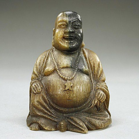 CHINESE CARVED RHINO HORN OF A SEATED BUDDHA: A very well carved figure of a Buddha with a joyous expression on the face and flanked by a pair of long lobes dressed in billowy robes opened to the chest and revealing an ample belly, and wearing a