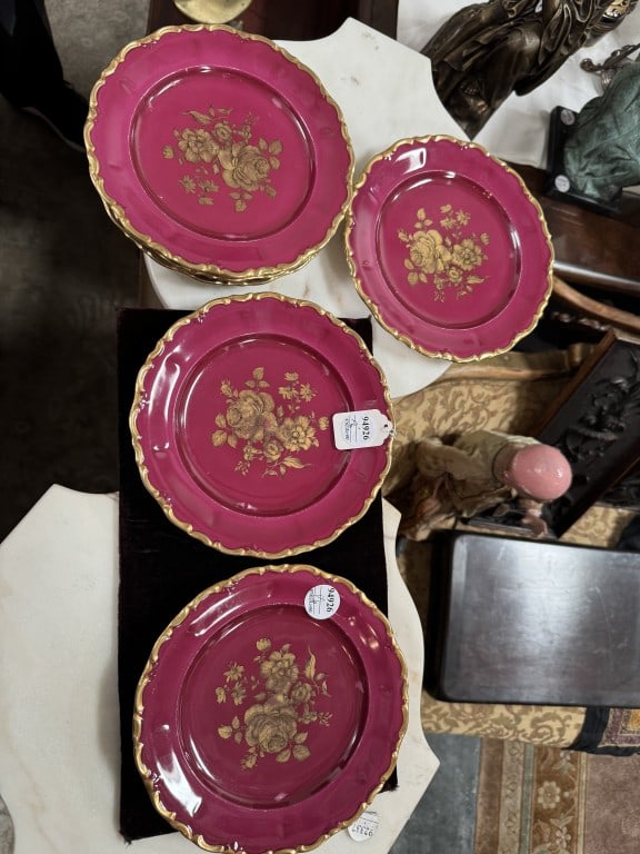 SET OF FOUR GILDED RED PORCELAIN DECORATIVE PLATES: Each of circular, scalloped shape, the wide borders are decorated in a vibrant. deep magenta ground. Each plate is centrally decorated with an intricate, gilded floral bouquet showcasing blooming rose