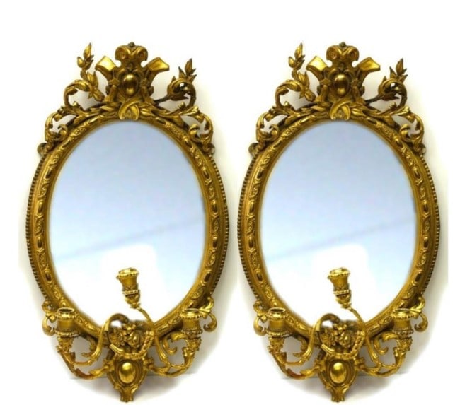 PAIR OF 19TH C EUROPEAN GILTWOOD FRAMED MIRRORS: Each mirror is of oval shaped, adorned with intricate details all over and flanked with three-branch candelabra under the mirror. H: 30 1/2 in.