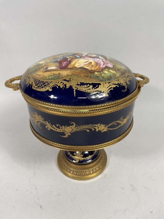 FRENCH SEVRES COBALT BLUE STEMMED CENTERPIECE: Raised on a curved, stemmed leg. Flanked by the round centerpiece with cover and two handles. Painted on the cover of a lover's scene with gilt details all over. Total Height: 8 3/4 in. Total Length (