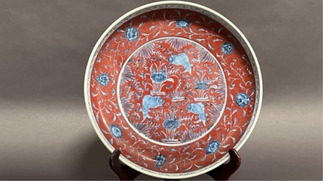 CHINESE MAROON RED AND BLUE SHALLOW DISH: Centrally depicting three fishes against a maroon ground with floral motif. Rim with a border of scrolls and inscriptions. H: 3 in. D: 16 1/4 in.
