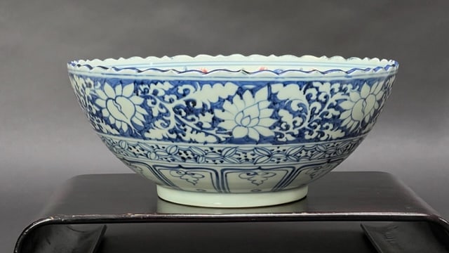 CHINESE BLUE AND WHITE BOWL: Raised on a short foot with foliated rim. Painted in the center of a figural scene with two generals. Surmounted by a band of floral motif in relief around the inner rim. H: 6 1/4 in. D: 15 in.