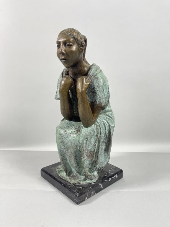 STUDIO BRONZE FIGURE OF A WOMAN: A studio bronze figure depicts a contemplative seated figure of a woman. Modeled as her hands clenched to the chest, evoking a sense of introspection and emotional depth. The bronze features patina on