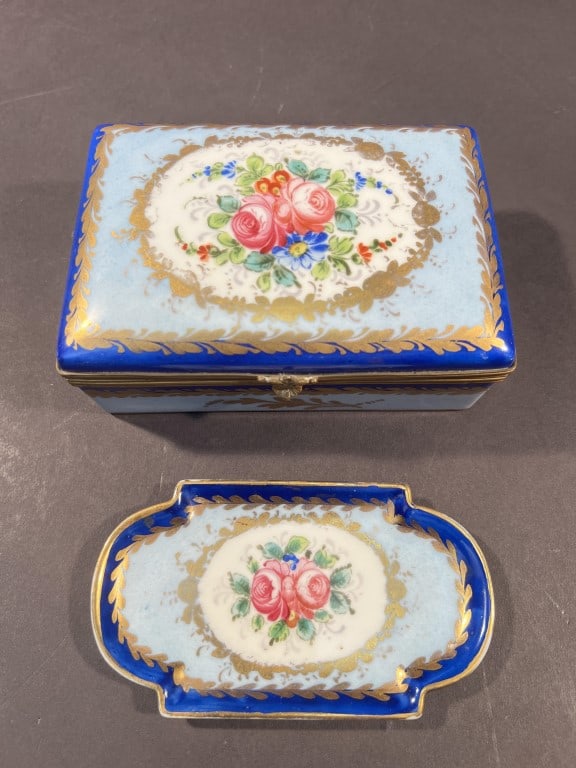 SET OF TWO HAND-PAINTED PORCELAIN ITEMS: Comprising of a matching set of a porcelain box and a plate. Both in overall two-tone colors of light blue body and dark blue border, and a central floral in cartouche design. Jewelry Box: L: 5 1/2