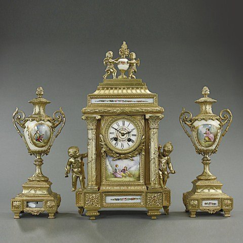 HAND-PAINTED FRENCH PORCELAIN GILT MANTEL CLOCK: A French hand-painted porcelain and gilt mantel garniture clock set. The central piece is a porcelain dime-shaped clock with a hand-painted porcelain plaque. Two porcelain pieces with gilt metal are o
