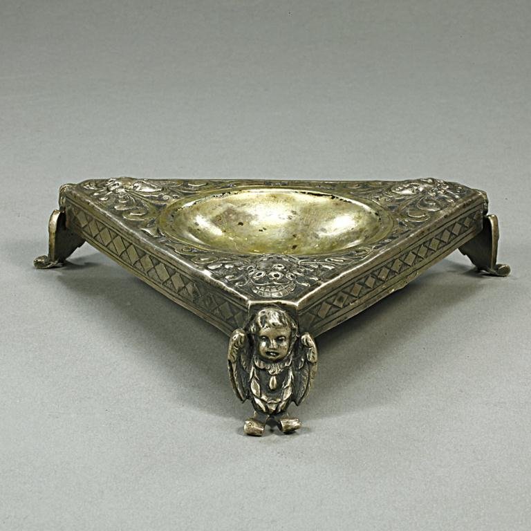 FRENCH SILVER PLATED TRIANGLE STAND: Three corners decorated with mythical creatures' heads with swirling hair are supported by cherubs as feet. L: 4 1/2 in.