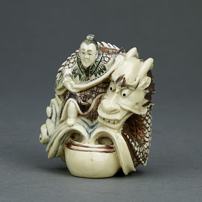 ANTIQUE CARVED IVORY NETSUKE: From the Private collection of Mr. Paul Siegal. Figure of a man holding a sign riding a curled dragon on crashing waves. H: 2 in.(5cm)