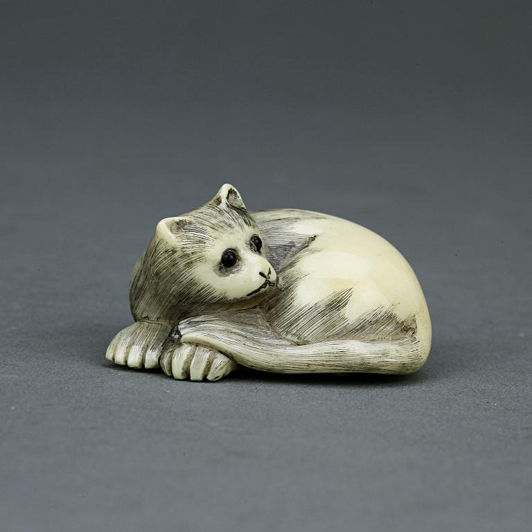 ANTIQUE JAPANESE CARVED IVORY NETSUKE: From the Private Collection of Mr. Paul Siegal. Figure of a recumbent cat. H: 7/8 in.(2cm)