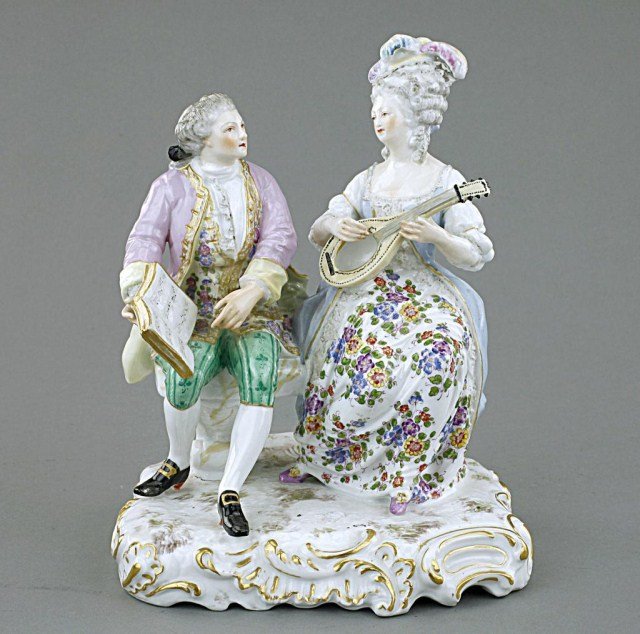 PORCELAIN FIGURAL GROUP OF TWO LOVERS: The figure of the lady is playing a banjo while the gentleman holds up a music book for her. Blue under-glaze mark on the base. H: 8 5/8 in.