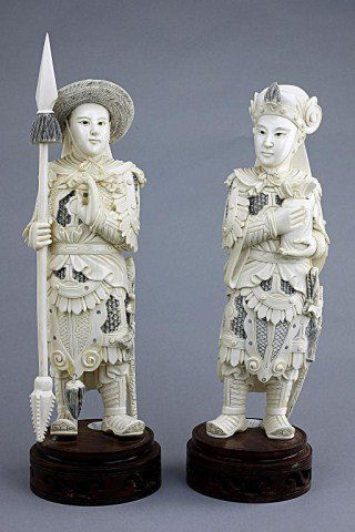 PAIR OF CHINESE CARVED FIGURES OF SOLDIERS: These two figures are dressed in armor with under armor in the style of pierced metal. One figure is holding a spear and the other is holding a bag of valuables. Both figures stand on a round carved w