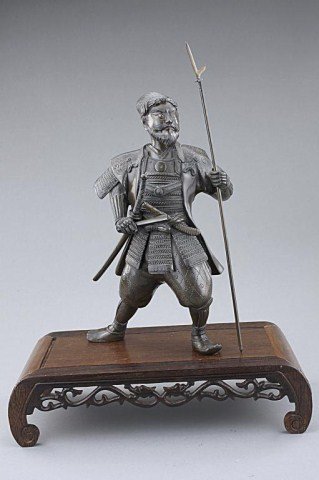 MEIJI PERIOD BRONZE FIGURE OF A SAMURAI: He stands proudly with a rather serious expression on the face, dressed in an elaborate armor and wearing a pair of sword tucked into his hakama while holding a long halberd in his left hand. Inlaid w