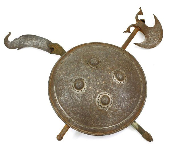 BRONZE SHIELD WITH AN AXE AND SWORD: The shield designed with four large bosse on metal ground etched with scrolling oriental pattern. L: 26 3/4 in. x D: 14 1/4 in.