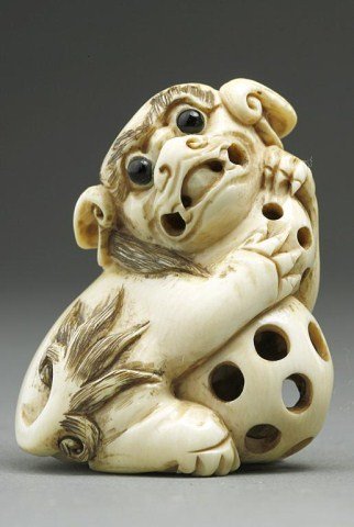ANTIQUE JAPANESE IVORY NETSUKE OF A KARASHISHI: Holding two reticulated balls, one with a loose ball inside. Inlaid eyes and stained detail. Signature under the left foot. H: 1 5/8 in.