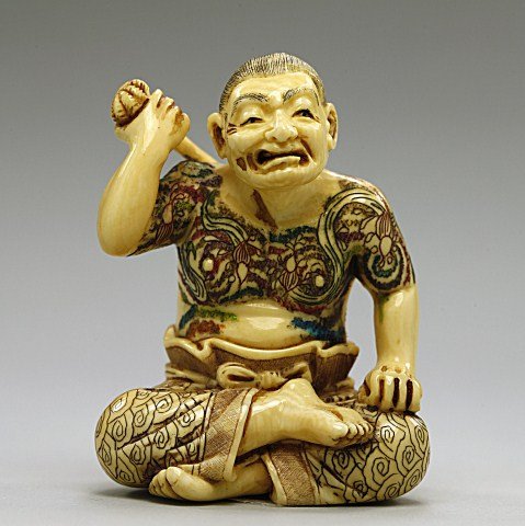 ANTIQUE JAPANESE POLYCHROMED IVORY NETSUKE: Of a man with a tattooed chest seated and scratching his back. Stained details. Signature underneath to read Garyo. H: 1 7/8 in.
