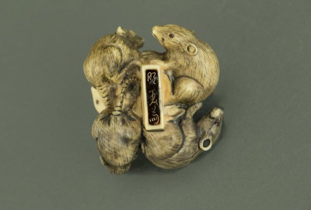 ANTIQUE JAPANESE CARVED NETSUKE OF RATS: With one white rat surrounded by four black rats. Staining on the four black rats and beetle on the white rat; inlaid eyes. Signature on inlaid dark stone strip on reverse side with a single hole unde