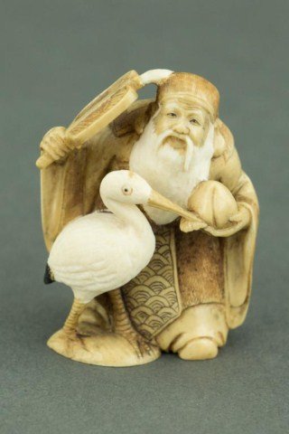 ANTIQUE JAPANESE IVORY NETSUKE FIGURE: Of Fukurokuju, one of the Seven Lucky Gods in Japanese mythology, and a crane. He is seen holding the peach of longevity in his right hand with a fan in his left. Stained ivory. Japanese characters to