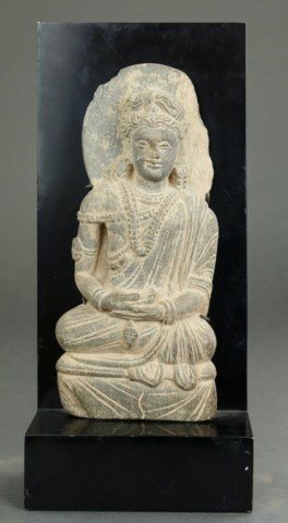 ANTIQUE CARVED STONE BUDDHIST DEITY: Seated with hands in dhyana mudra. Wears a heavily draped robe and a multi-strand necklace. Fragmented from a larger stone piece. Mounted on a stand. H: 15 in.