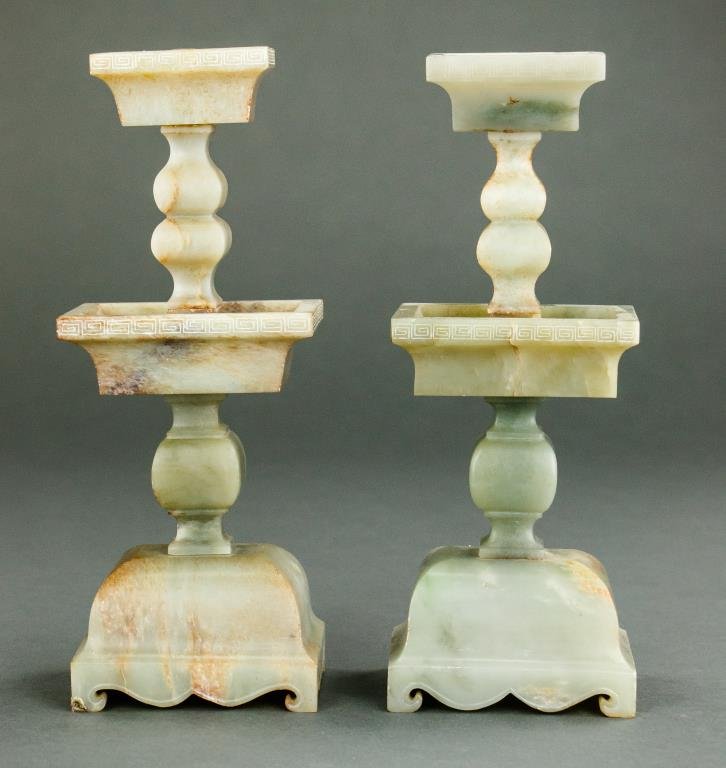 PAIR OF CELADON JADE CANDLESTICKS: In square form, the shaft carved with rounded nodes. Key fret band around the socket and the bobeche. Base raised on four short hoofed feet. H: 10 1/4 in.