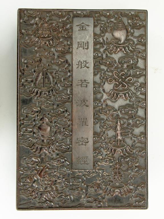 CHINESE HAND CARVED HARDWOOD SUTRA BOX: The eight Buddhist auspicious symbols carved in relief on the top and sides of the box among swirling clouds; inscription on rectangular plaque in the center of the lid. H: 4 in., L: 15 in., W: 9 3/4 