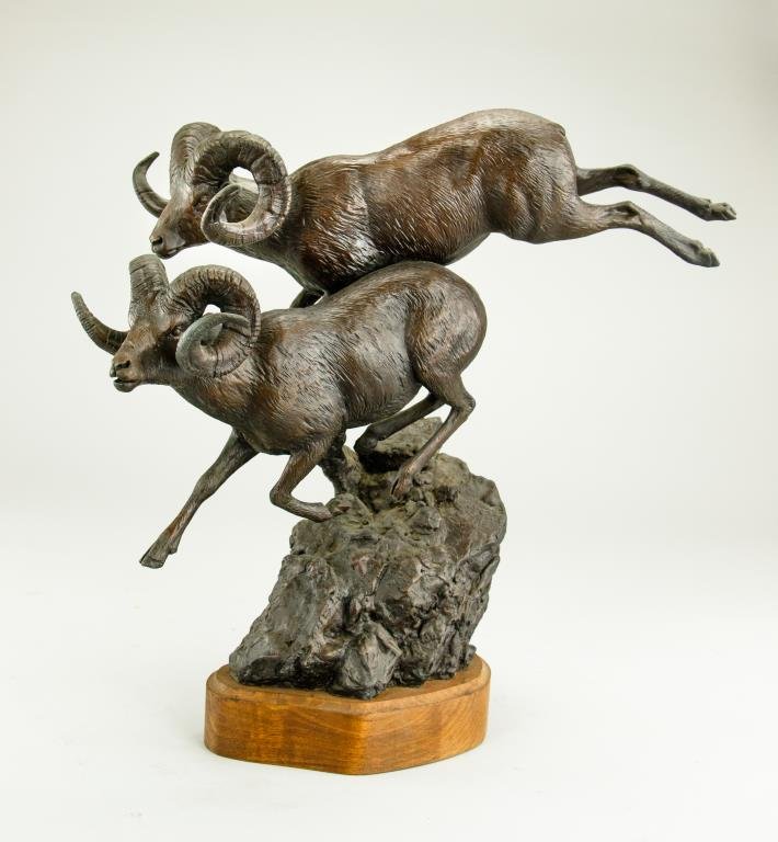 BRONZE FIGURE OF TWO RAMS LEAPING OFF ROCKS: BRONZE FIGURE OF TWO RAMS LEAPING OFF ROCKS Rams are in lively leaping position and attached to wooden base. Inscription to read "Jack D Putnam 1976". 20th century. H: 16 1/2 in.