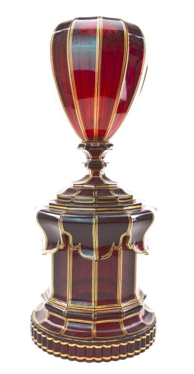 19TH CENTURY BOHEMIAN GLASS CENTERPIECE: In deep red color, the sides faceted. On fluted round base and with gilt painted line details all over. H: 18 3/8 in.