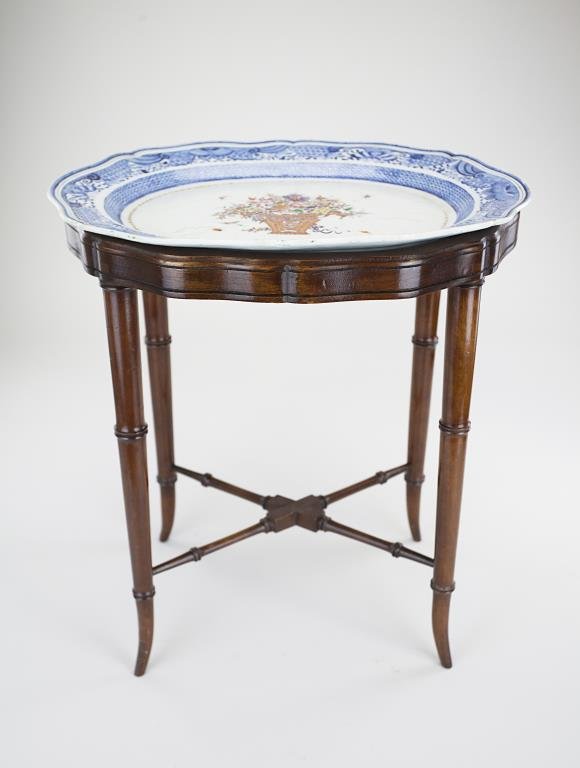 18TH CENTURY CHINESE PLATTER SET AS A TABLE: The center of the platter painted with a basket overflowing with flowers and the rim with border of insect motif. Raised on four wooden legs connected by a cross stretcher. H: 19 in., L: 17 3/8 in., W