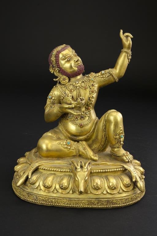 ANTIQUE GILT BRONZE MONEY GOD WITH STONE INLAY: Reclined with one arm outstretched and one knee propped on a deer rug atop a single lotus pedestal. He wears a floral garland around his body and has his hair and beard in tight curls. H: 9 7/8 in.