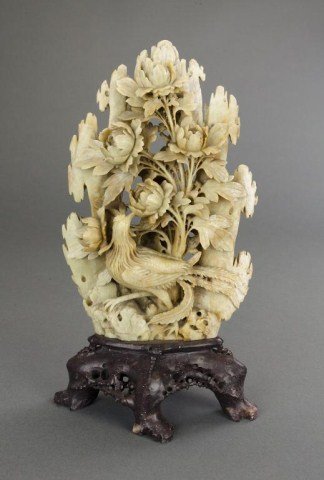CHINESE CARVED SOAPSTONE OF A PHOENIX AND FLOWERS: Reticulated boulder of a phoenix gazing back at a bunch of flowers. On a carved wooden stand. H: 12 1/4 in.