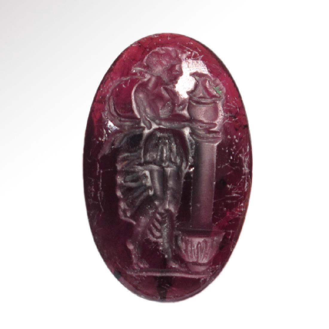 Roman Garnet Intaglio, c. 2nd-3rd Century A.D.: Roman Garnet Intaglio, c. 2nd-3rd Century A.D. Carved with a lady wearing a tight fit pleated dress, placing a votive bell-crater over a column. Size:2.4 cm L - 15/16 inches Material:Garnet Culture:Ro