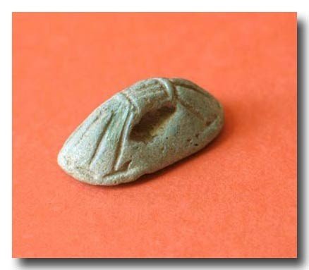 Egyptian Faience Seal, 18th Dynasty, 1504-1450 B.C.: Engraved with standing figure of Anubis, with a feather behind and a lotus flower in front, bowed suspension loop, in the form of a bunch of reed. Material:Faience Size:3.6 cm. L.- 1 7/16 inches Free