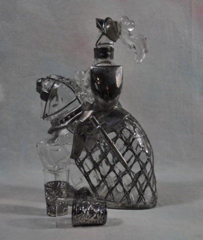 Sterling Clad Art Deco Figural Decanter: Knight on horseback, fitted sterling frame stamped 950 detailing the figures armor and horses regalia, together with: 2 shot glasses, also framed in sterling stamped 950, featuring roses in full bloom