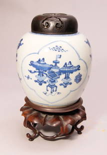 Ingwertopf Kangxi Periode: Porzellan. Holz. Unterglasurblaue Bemalung mit Dekor von Vasen und Gefäßen, gerahmt von vierpassigen Medaillons, seitlich begleitet von Blütenranken. Holzdeckel und -basis geschnitzt. H. 28 cm (ges