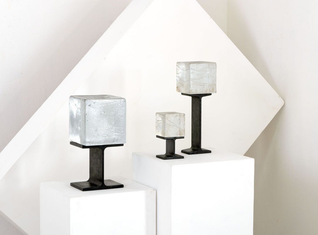 Christer Sjogren: Tre blocchi in vetro stampato e rifinito alla mola su supporti in ferro laccato. Prod. Lindshammar, Svezia, anni '60 Firma incisa ed etichetta adesiva parzialmente leggibile. cm 40x19x19, cm 42x13x13,