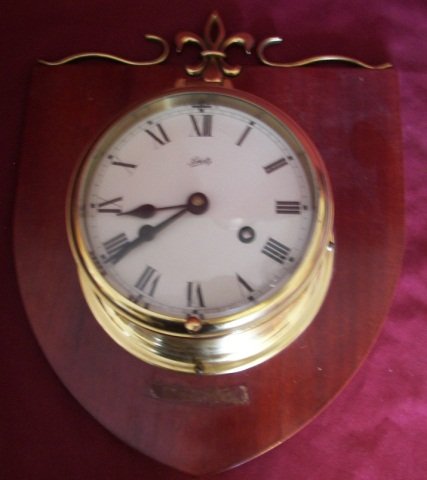 Vintage Schatz Brass Ships Clock: (6047) Vintage Schatz Brass Ships Clock with Key, Made in Germany, Strikes the Hour and the Half Hour, Serial Number E66065-J, Mounted on Mahogany Shield Shaped Plaque with Fleur-de-lis Brass Trim, 6"