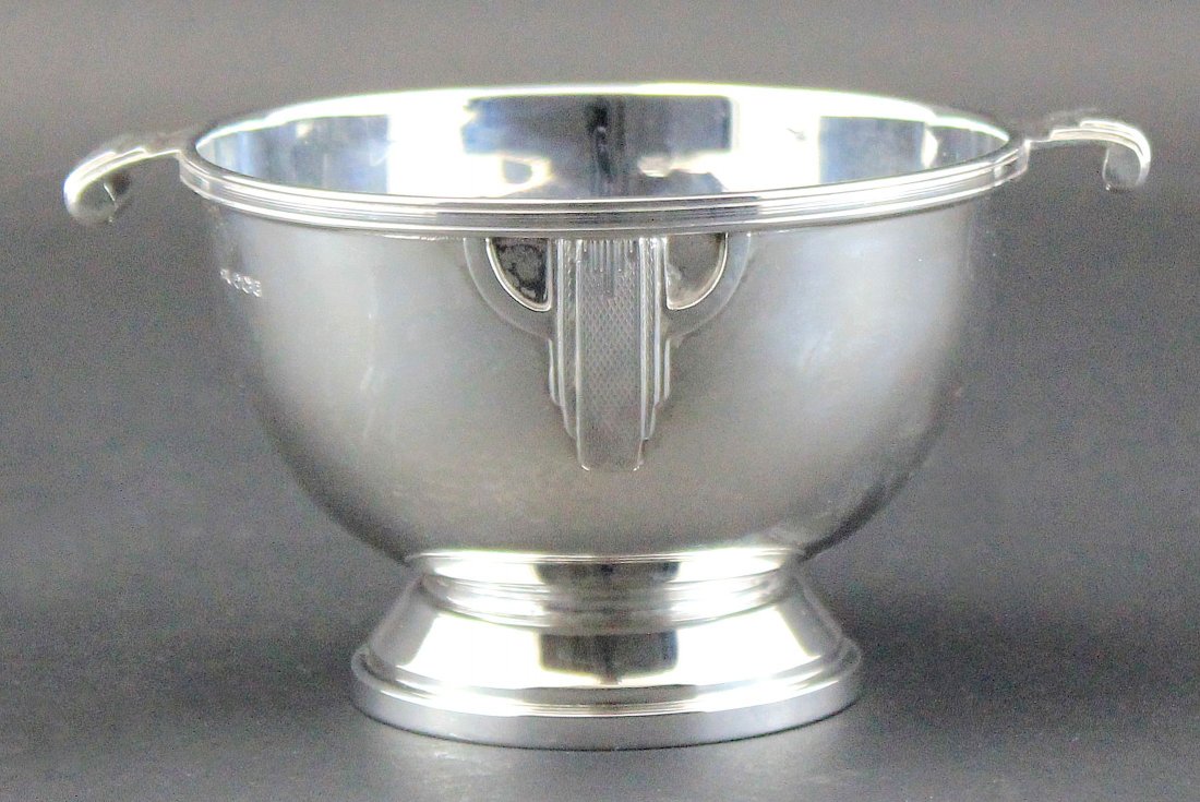 GEORGE V SILVER BOWL: SHEFFIELD, 1947, Walker & Hall, The Art Deco inspired bowl raised on a stepped circular base, mounted with twin handles and engine turned appliques. 5.25 in, 13.5 cm width over handles. 185 grams.