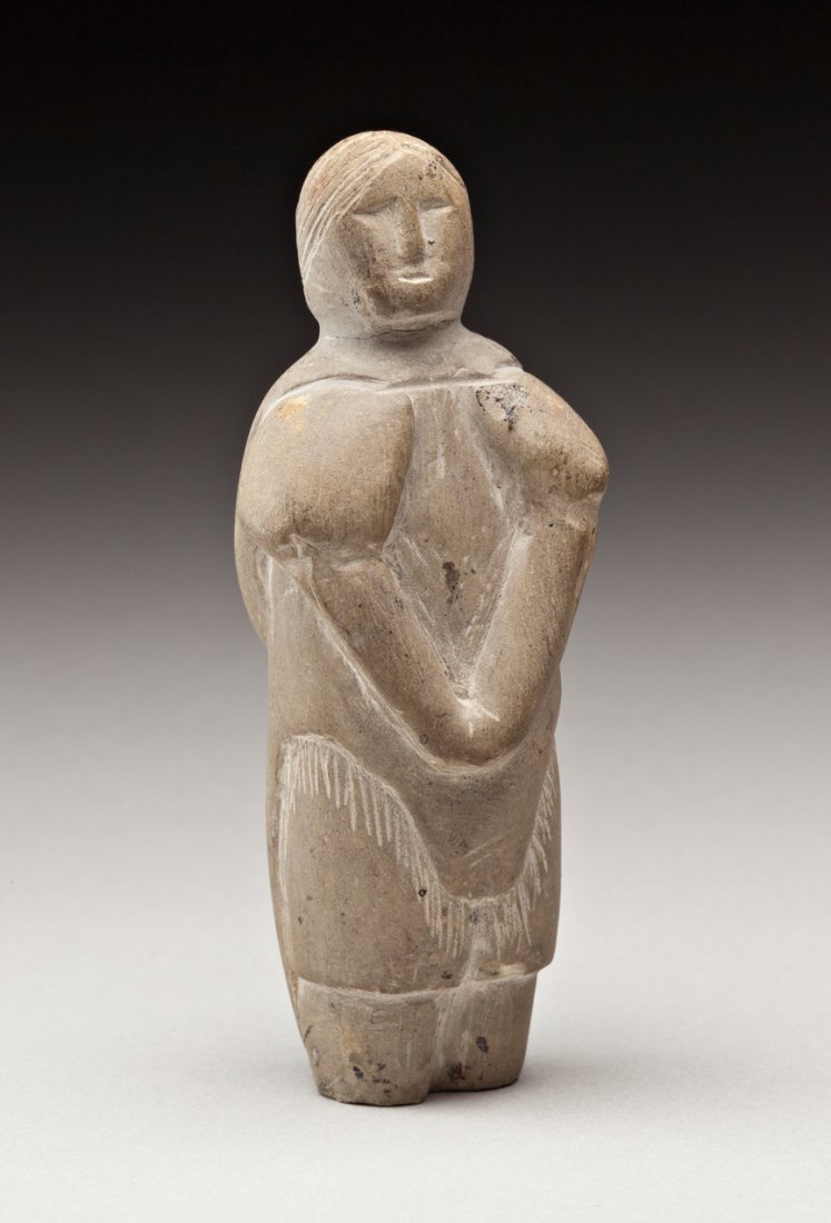 Unidentified artist: Probably Kugaaruk (Pelly Bay), Standing Woman, probably 1950s, light brown stone, 2.75 x 1 x 1.25 in, 7 x 2.5 x 3 cm. --- CATEGORIES: Inuit, Eskimo