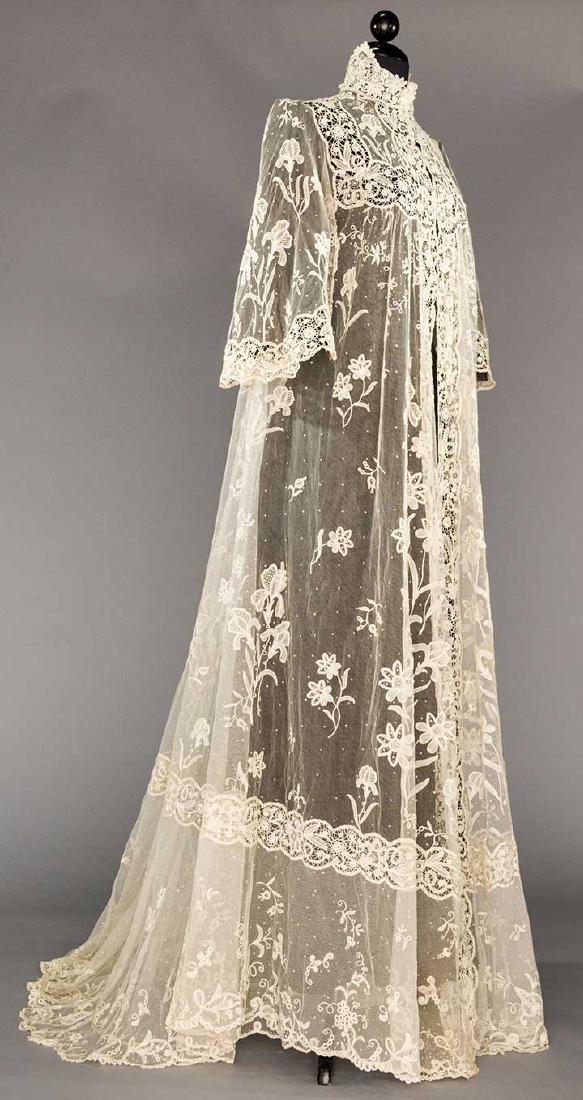 BRUSSELS LACE PEIGNOIR, 1905: White cotton tulle w/ floral appliques of iris, lillies-of-the-valley, etc., edging & insertions of Brussels lace guipure, bell sleeves & trained, B 34", L 63"-80", excellent.