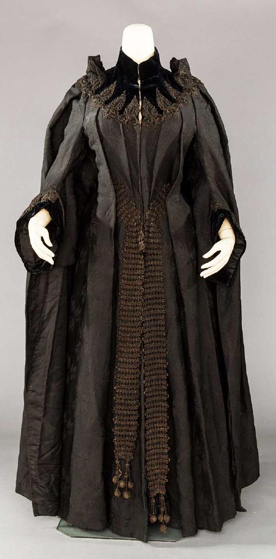 WOOL DOLMAN BUSTLE COAT, PARIS, MID 1880s: Black wool leaf patterned damask, cuffs & yoke of black velvet w/ black cord appliques, label "Cacard & Raffin", knife pleats to CF & CB, large CB applique anchors back pleats, long corded CF bands w/