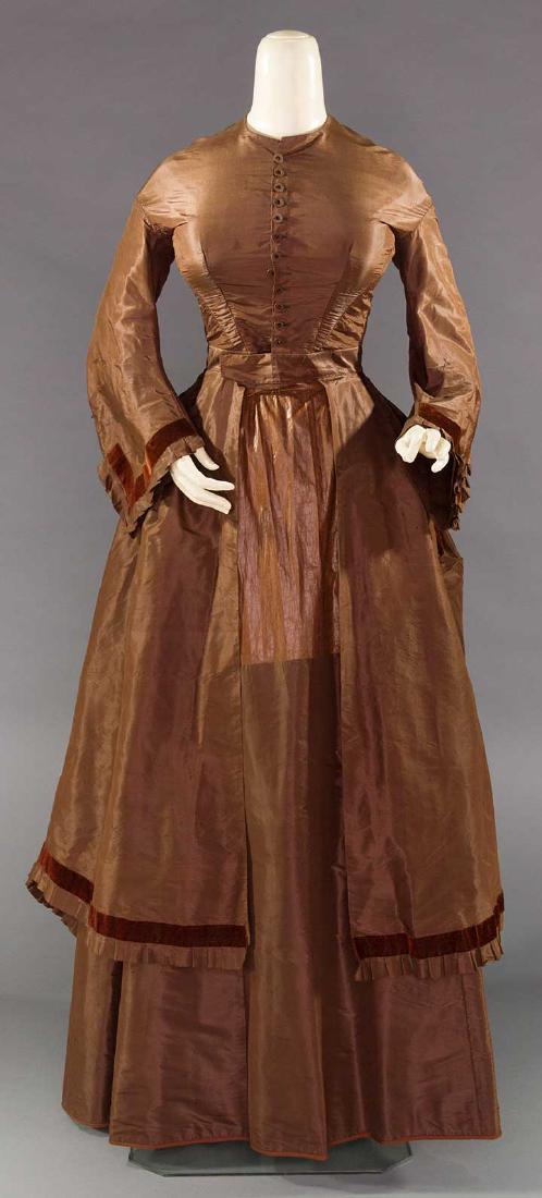 CHOCOLATE POLONAISE AFTERNOON DRESS, c. 1868: Silk faille 2-piece, velvet trim, Polonaise bodice w/ transitional sleeves, 12 small silk covered CF buttons w/ jet centers, attached long open-front skirt w/ partial bustle, under-skirt of highly gla