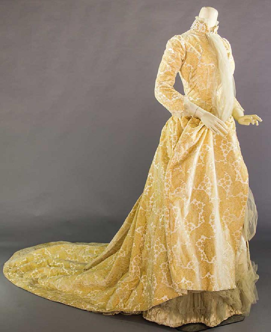 A. FANET WEDDING GOWN, PARIS, 1880s: 2-piece, light gold velvet flowers cut to ivory satin, pearl-trimmed high band collar, chiffon panels at CF bodice & trained bustle skirt, labeled petersham "A. Fanet….Paris", B 32", Skirt L 59"-103