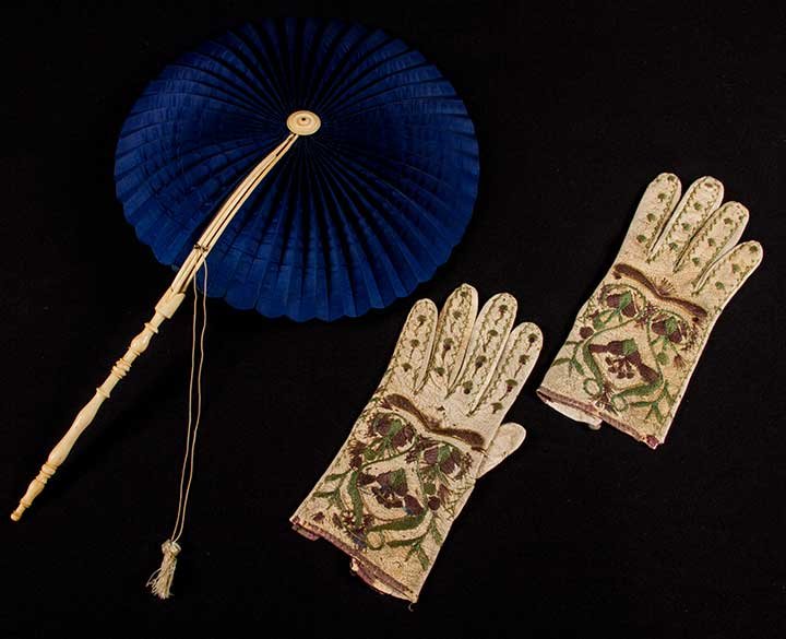 EMBROIDERED GLOVES & COCKADE FAN, 18TH C: 1 pair goatskin leather gloves, brown & green floss embroidery, Portugese? Date?, L 8.75", (dirty, many pin holes = embroidery losses) fair; 1 fan w/ carved bone guards & stick, dark blue glazed linen