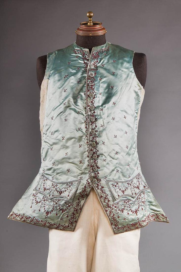 GENT'S BLUE SILK WAIST COAT, 1770-1780: Sky blue satin, brown tambor stitch of tassels, ribbons & bows, CH 44", L 31", (front lining panels & back replaced in 20th C., minor very small stains) very good.