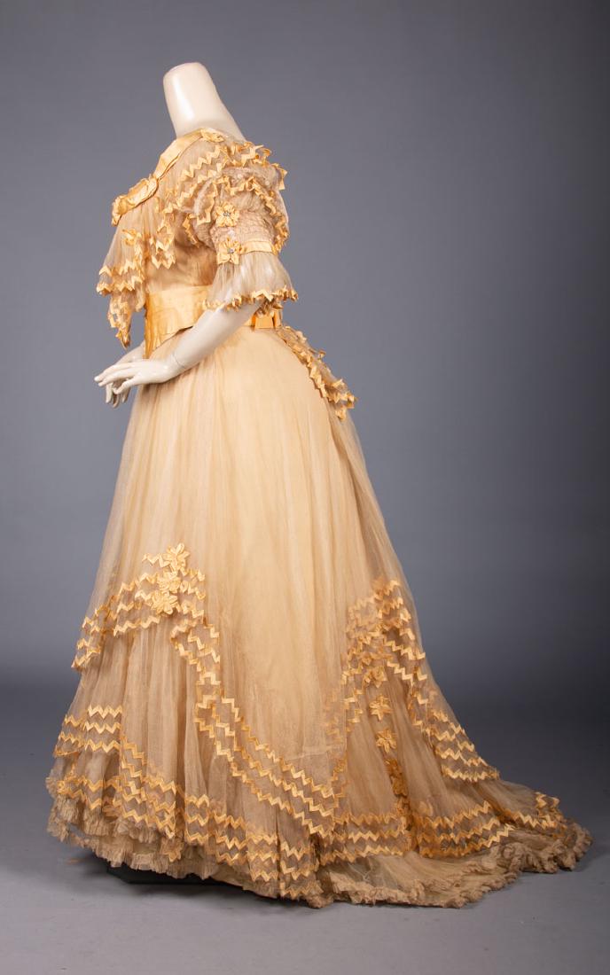 YELLOW SILK TULLE BALL GOWN, LATE 19TH C: Lemon yellow silk satin 2-pc dress w/ ric-rack trimmed net overdress, rhinestone buttons on sash, B 40", Petersham 30", Skt W 32", CFL 40", CB L 50", (stains at CF & B bow, side seams let out, W alter