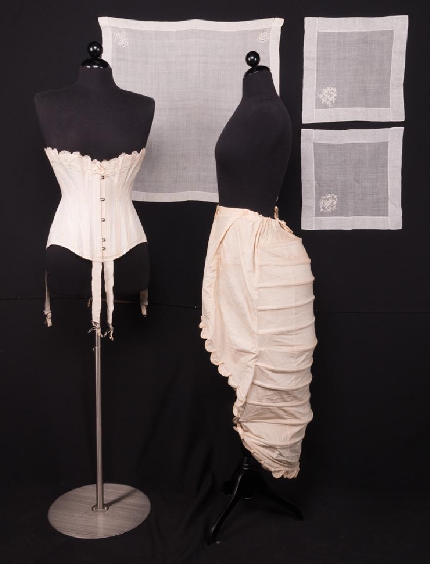 WOMENS CORSET, c. 1910 & LOBSTER TAIL BUSTLE, 1870s: 1 white strapless corset w/ attached garters B 38", W 27", CF L 12", (small light stain) very good; 1 muslin covered bustle, scalloped hem & CF buttons, L 13-36", (missing a button, dirty) very good;t