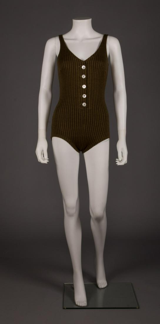 RUDI GERNREICH STRIPED BATHING SUIT, 1960s: Khaki green & black pinstripe w/ 5 M.O.P. buttons at CF opening, label "Rudi Gernreich", B 32", W 24", H 32", (small moth hole to left of 2nd button, 0.25" repair at left H) good. Identical suit in co