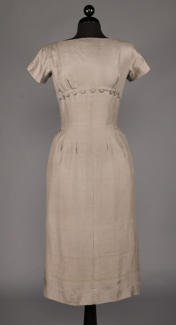 SUZY PERRETTE AFTERNOON DRESS, LATE 1950s: Dove grey silk shantung 1950s dress w/ short sleeve, curved high W in front w/ dart & button detail, 2 ss pockets, V-back & CB zipper to deep pleat, label "Suzy Perette, B 36", W 26", H 36", L 47.5",