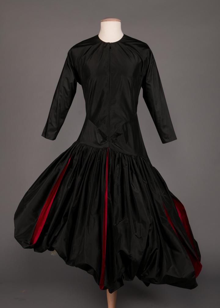 MME GRES MONASTIC EVENING GOWN, 1978: Black silk taffeta monastic evening gown w/ fitted bodice, zipper at CF to high neckline & drop W to gathered asymmetric infinity skirt w/ slits to crimson lining, label "Gres", B 34", W 28", L 48", (